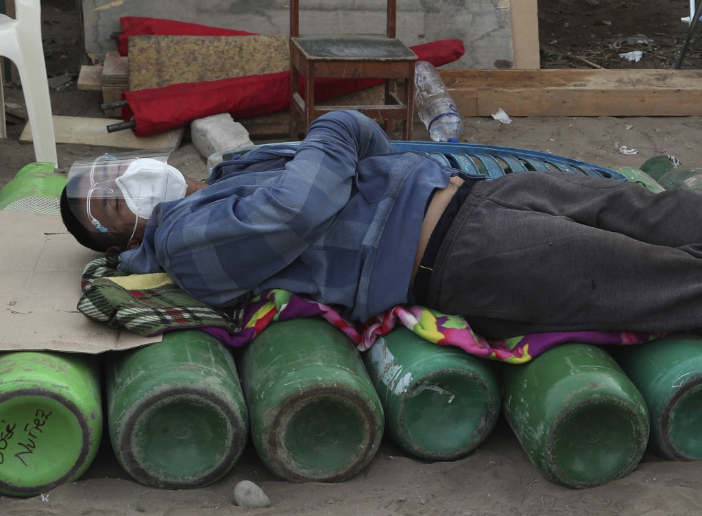 A man sleeps on top of empty oxygen cylinders, waiting for a shop to open to refill his tank, in the Villa El Salvador neighborhood of Lima, Peru, early Thursday morning, Feb. 18, 2021. A crisis over the supply of medical oxygen for coronavirus patients has struck nations in Africa and Latin America, where warnings went unheeded at the start of the pandemic and doctors say the shortage has led to unnecessary deaths.