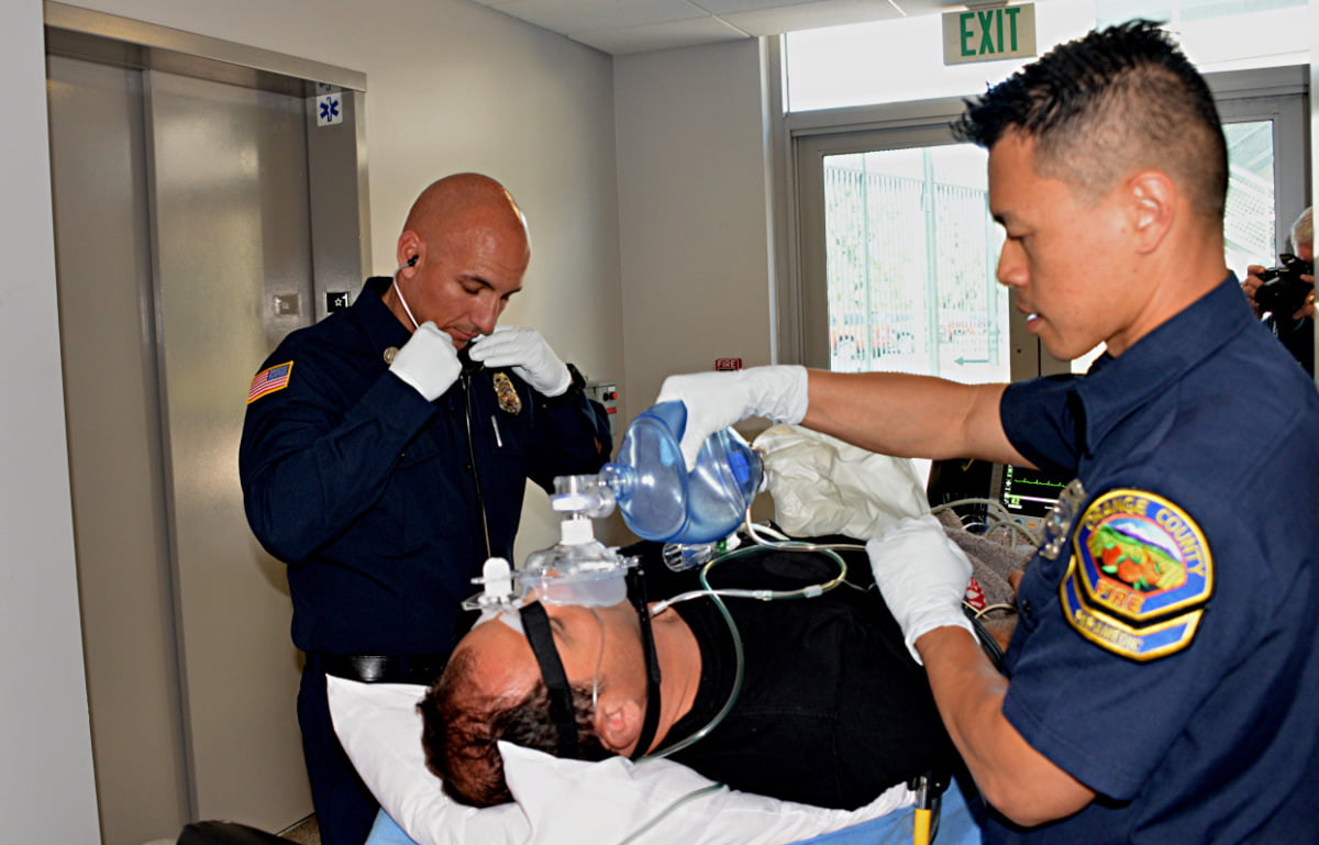 Two men in uniform use a medical airway device on a man in a stretcher.