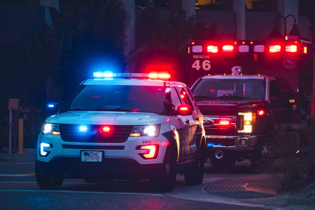 A police SUV and an ambulance shown at night with its lights on.