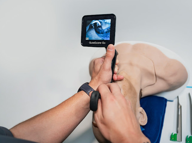 Person using a GlideScope Go video laryngoscope on a medical airway manikin, showing glottic view on the device screen.